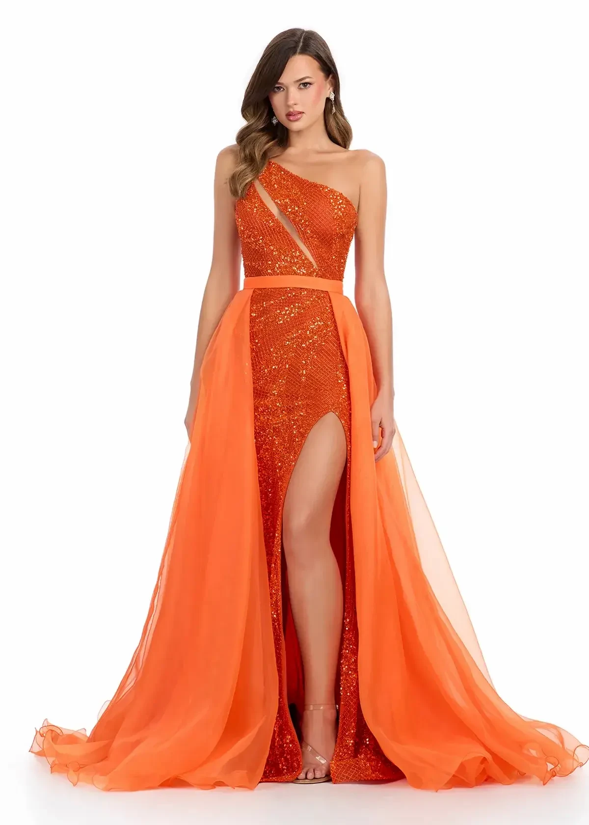 Model is wearing an orange one shoulder prom dress with an organza overskirt 