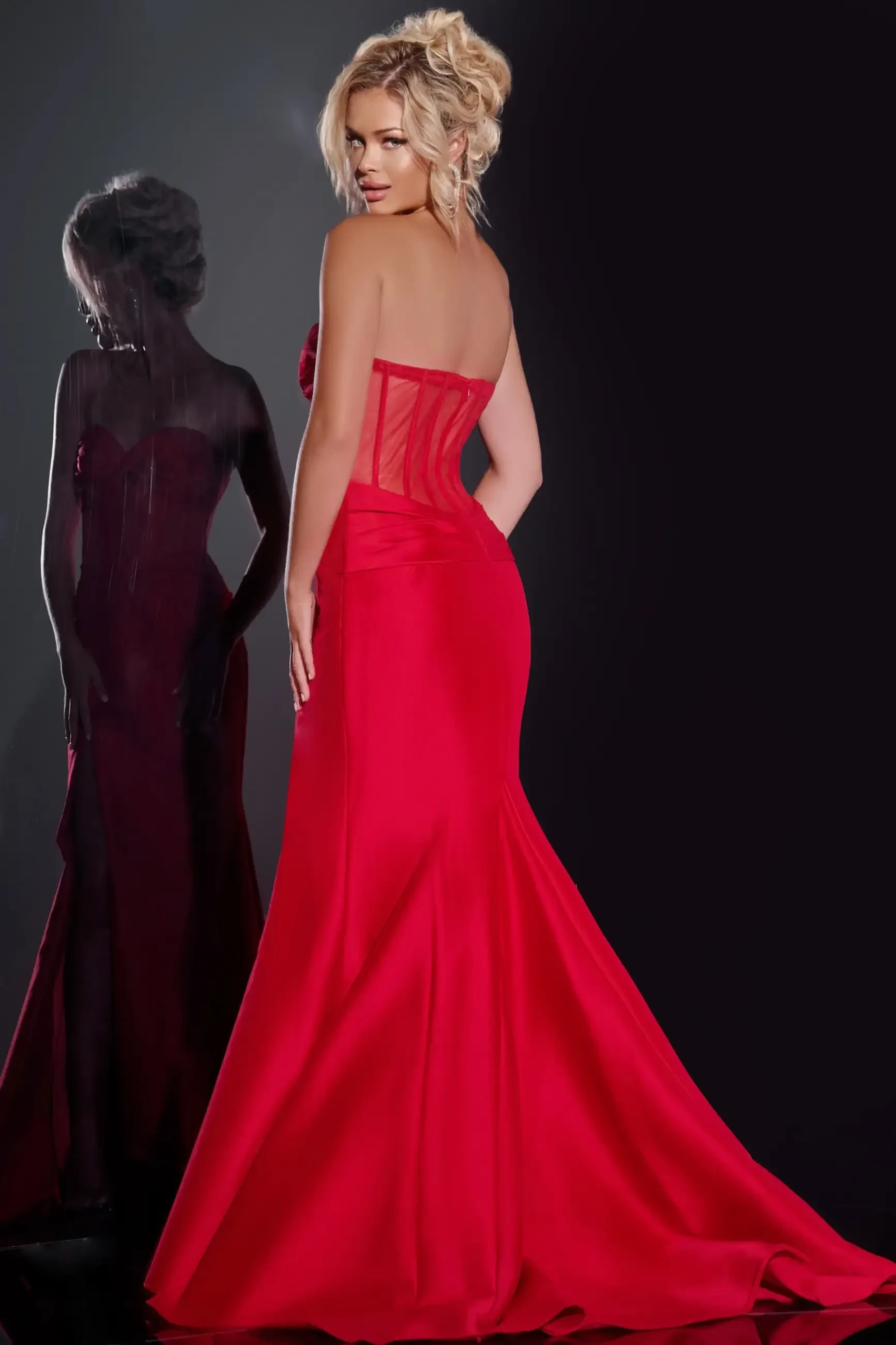 Model is wearing a strapless red fitted prom dress with a corset bodice and thigh high slit