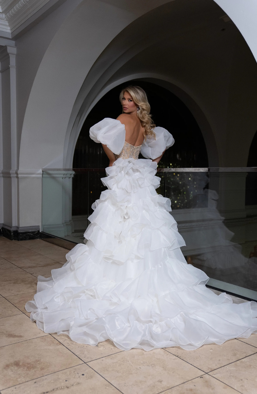 model is wearing a champagne glittery floor length evening gown with an organza overskirt and detachable sleeves